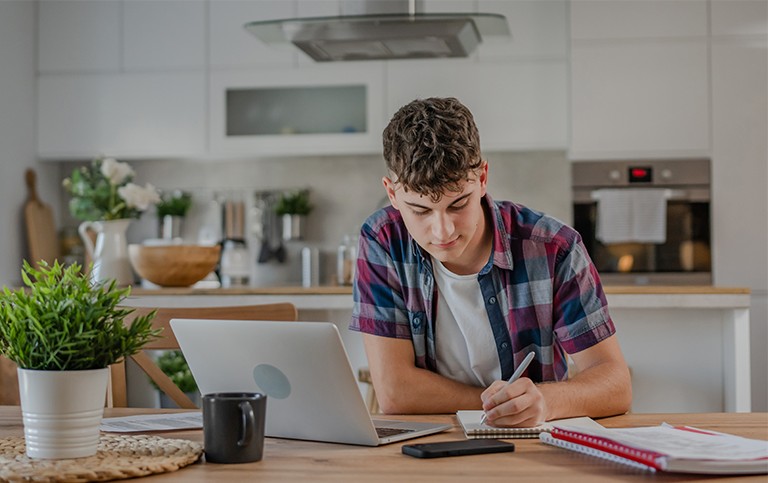 An adolescent boy taking notes at the kitchen table