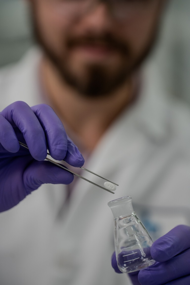 A research and development employee holding a vial and a 25 mg pill with forceps