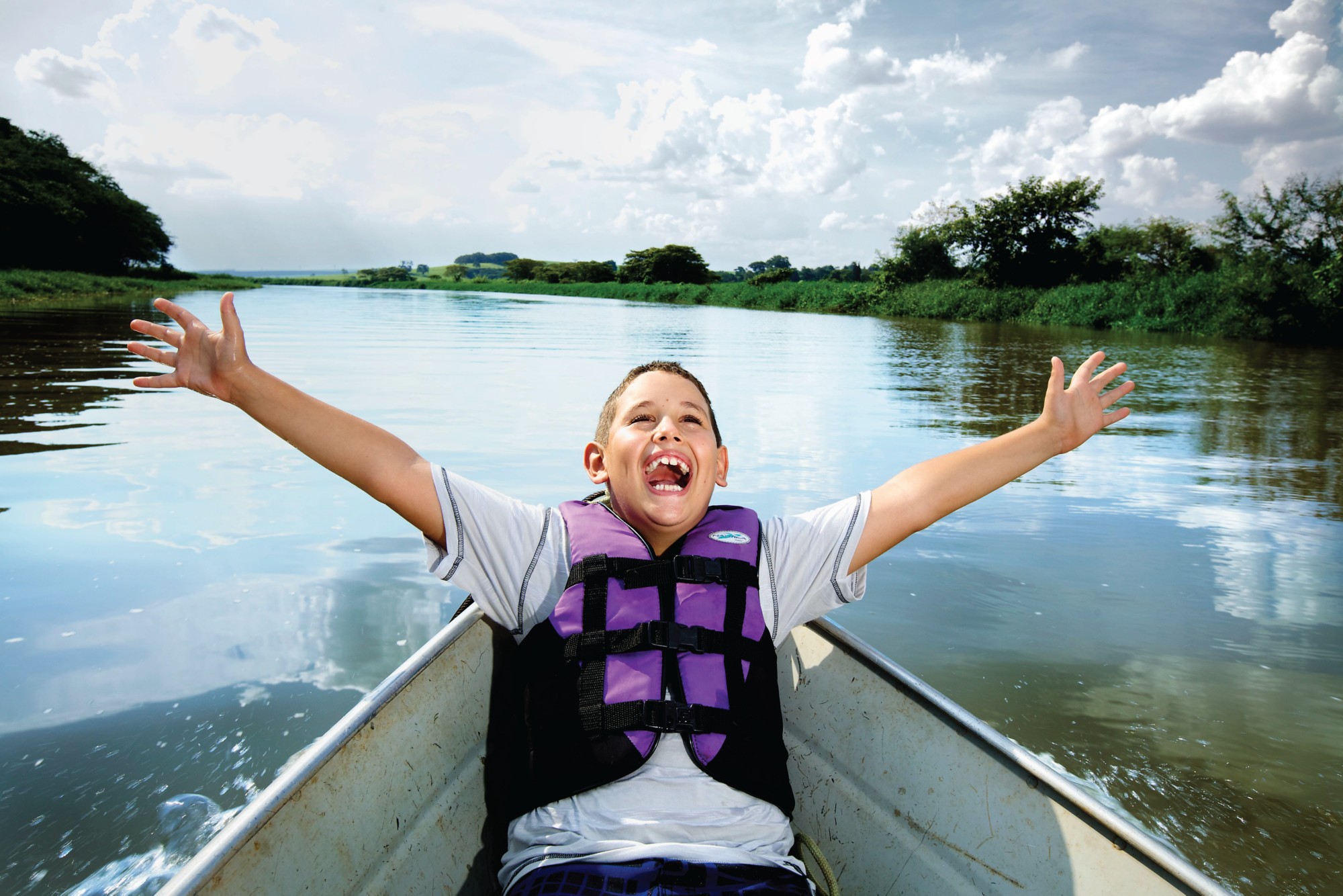 Ett barn med stort leende som sitter i en båt med armarna utsträckta