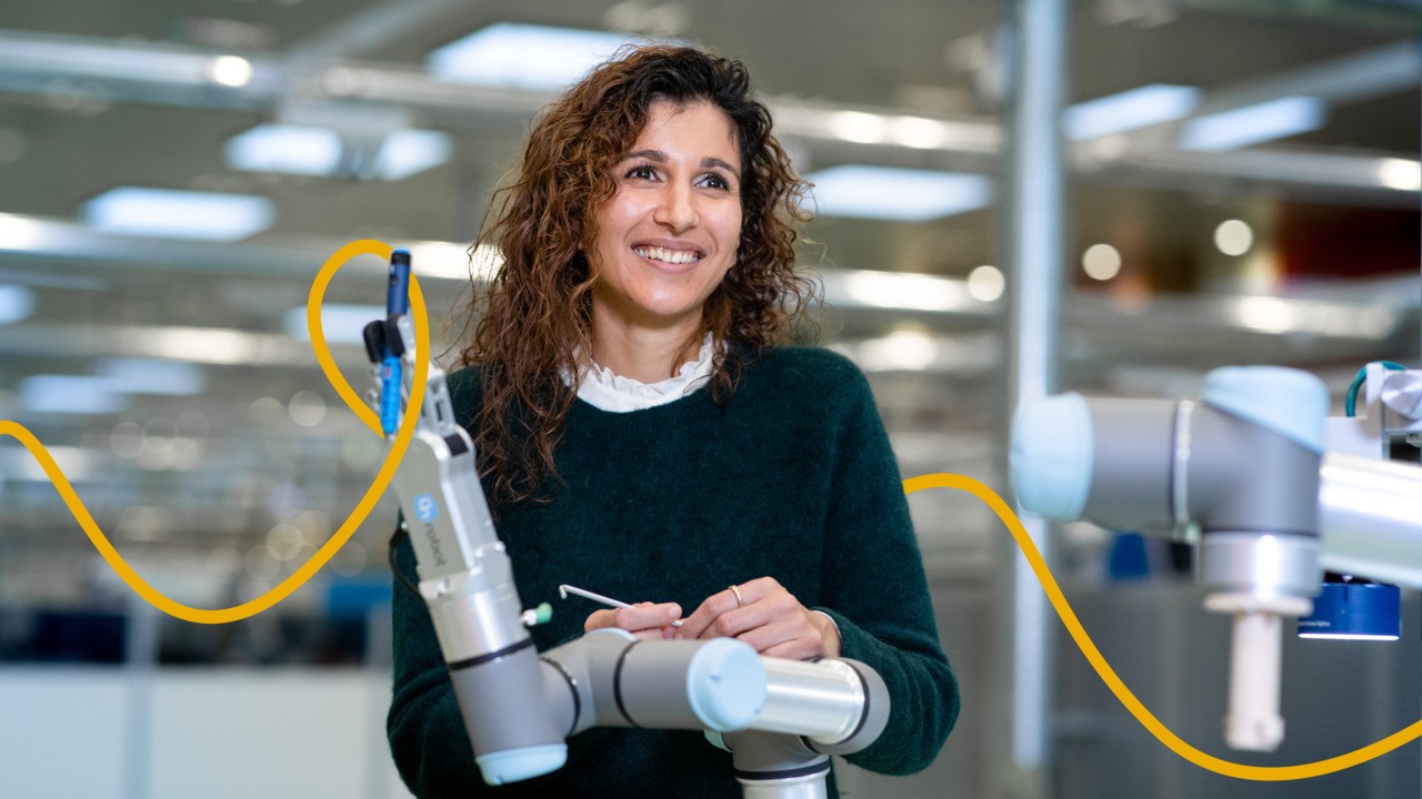 Roa is standing in front of a robot arm. She is holding a tool in her hand, used to adjust the robot arm.