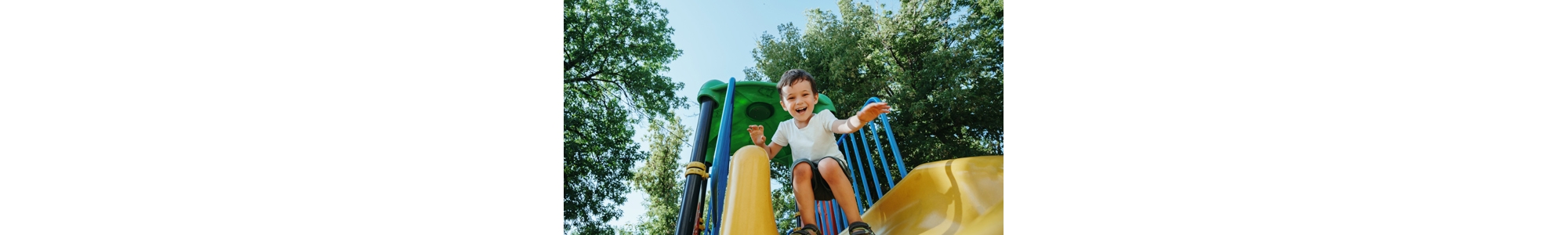 happy preschooler boy playing on a slide on the playground in summer