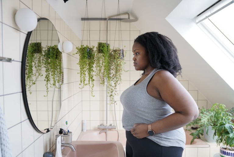Woman living with obesity looking at herself in the mirror in the bathroom